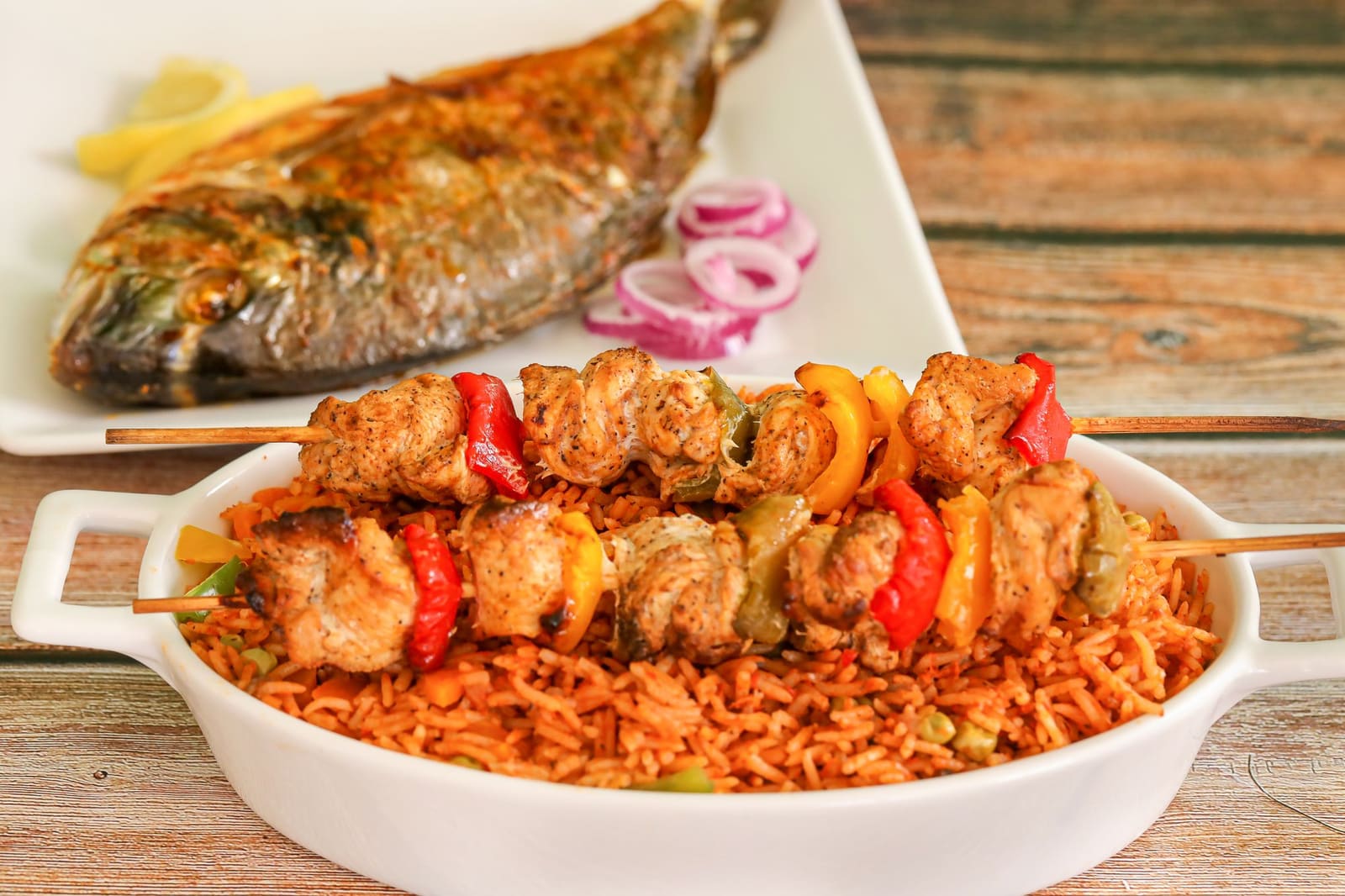 Riz jollof servi avec des brochettes de poulet et un poisson grillé